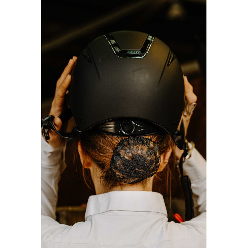 Equitheme Dentelle black lace hairnet worn as a bun by a rider putting on her helmet – equestrian competition hairnet at Ekkivibes