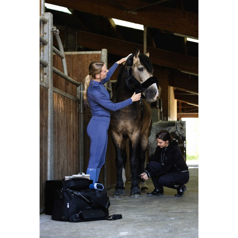 Woman grooming a horse wearing Elsa JTM blue riding breeches by Equitheme – equestrian lifestyle at Ekkivibes